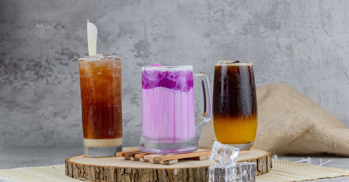 A collection of assorted beverages including coffee and a pink drink, served on a rustic board with ice cubes.